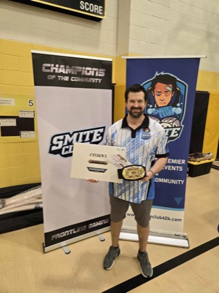 Ben McDonald holds the Best Overall championship belt and certificate between the Smite Club and Champions of the Community banners at Scorched Earth Open 2026